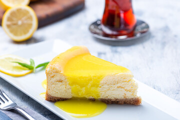 A slice of lemon cheesecake with tea in traditional Turkish teacup and half a lemon showing in the background