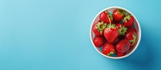 Delicious berry dessert featuring fresh ripe strawberries in a cup on a blue paper background viewed from the top with copy space image