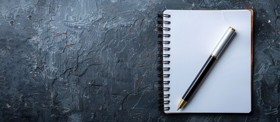 Display a pen on gray and black textured background with a blank notepad having empty pages for a copy space image