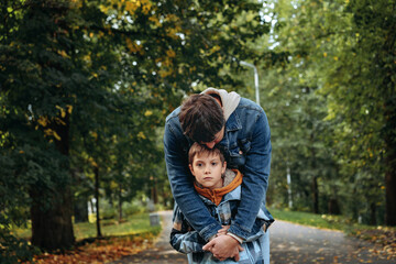 Caucasian man hugging his son in autumn park supporting sad boy