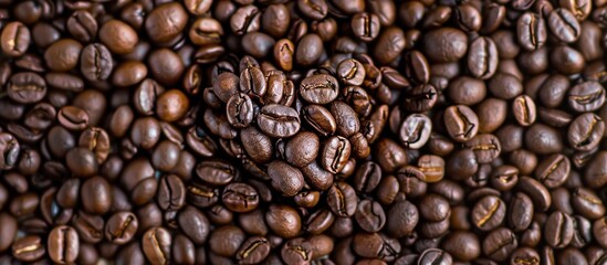 Fototapeta premium Close up of a heart shaped formation created with coffee beans on a background of roasted coffee beans emphasizing the concept of International Coffee Day with copy space image