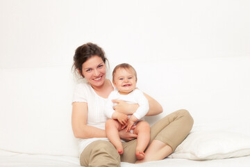 Happy mother playing with baby on white sofa