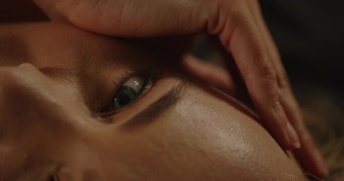 Macro of an attractive woman sensually caressing her face while looking at camera and moaning