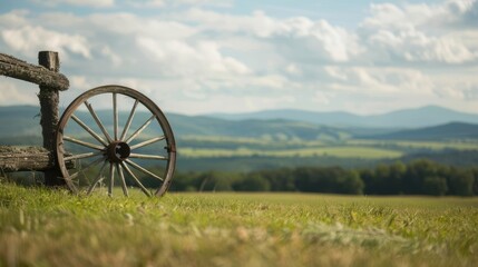 Fototapeta premium Vintage wagon wheel leaning against a wooden fence overlooking a scenic rural landscape.