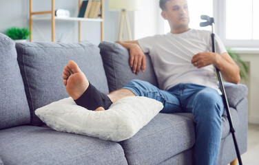 Obraz premium Close up shot of a man bandaged broken leg as he sits on a couch at home. Medical treatment and rehabilitation process required for trauma and injury, highlighting the challenges of recovery at home.