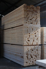 Wooden boards after processing are stacked in large piles in the warehouse of a woodworking plant
