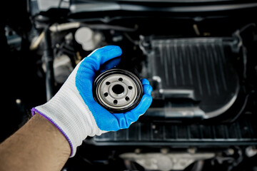 Top view of gloved man's hand holding the oil filter of a car. Close-up of a new oil filter in the...