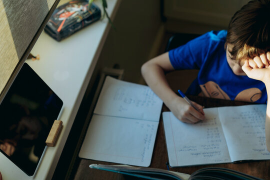 stressed tired boy doing homework at home at the desk by the window.