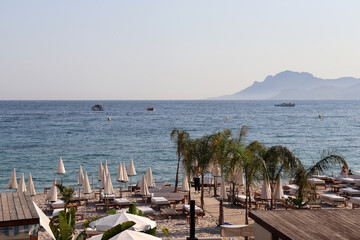 Parasols and palm trees on the beach at La Croisette in Cannes in the south of France with mountains in the background