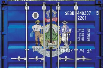 Maine US state flag depicted on metal doors of shipping cargo container outdoors in docks area...
