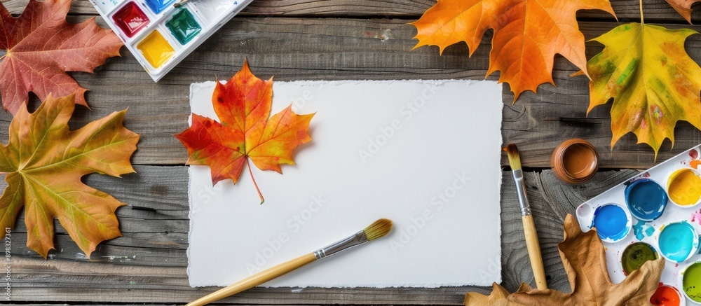 Poster autumn themed artist s workspace with a sheet of paper watercolor paint set brush and autumn leaves 