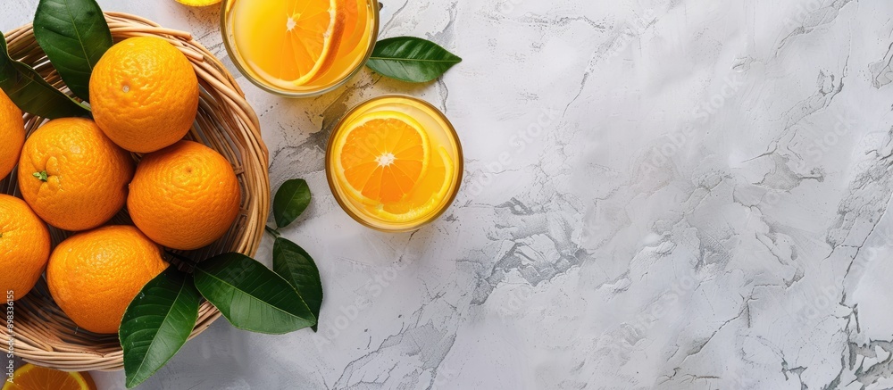 Poster Top down view of a basket containing oranges with leaves accompanied by a glass of orange juice set on a bright background with ample copy space image