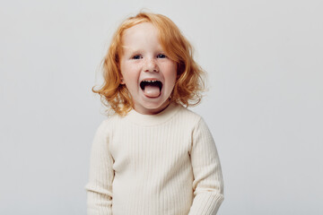 Funny redhaired girl making faces in front of white background, child portrait with humorous...