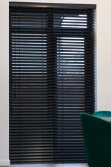 Interior with black wooden blinds on full height window, perfect for light control and privacy. Complemented by a chic marble table and plush green chair, wood blinds add functionality to a room. © Astibuk