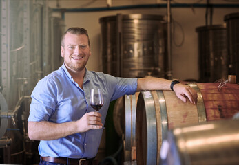 Wine, distillery and portrait of man with glass for alcohol production, aging and pride in job. Happy, business owner and face with confidence by barrel for manufacturing, industry and process
