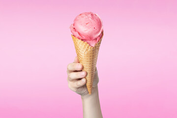Woman's hand holding waffle cone with strawberry ice cream on pink background