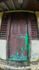 Vintage wooden door with peeling green paint, featuring an air ventilation grill, showcasing the charm of an old building.
