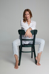 Full length image of a young woman posing on chair, isolated white background. Black and white image.