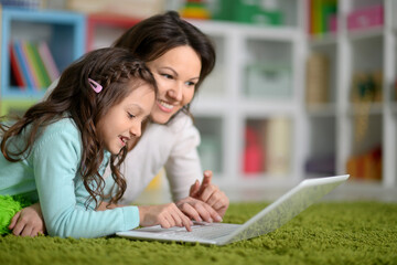 Happy laughing mother and little cute daughter using laptop