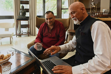 Mature men watching video online on laptop during meeting in the living room