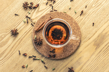 Cup of freshly brewed black tea, different types of spices on wooden table.