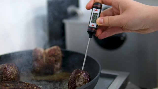 Checking oil temperature inside pan. Ribeye steak with rosemary, garlic and blurred meat thermometer to check right steak temperatures. Cooking pan seared ribeye steak in Korean granite
