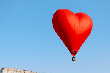 red heart balloon soaring above white building with red roof on a sunny day