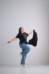 businesswoman joyfully tosses her blazer in the air while wearing a black top, blue jeans, and a pearl necklace. The minimalist background emphasizes her carefree and confident spirit.