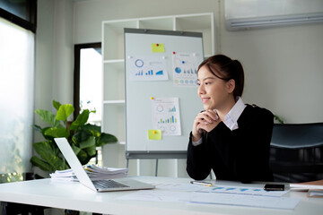 Naklejka premium Young Business Woman Working at Desk with Laptop in Modern Office, Analyzing Data and Charts, Professional and Focused