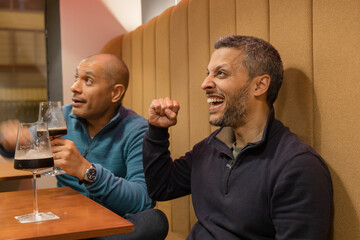 Two men are sitting at a table, laughing and holding up their hands