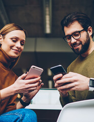 Two young carefree users chatting with follovers in social network via telephones, hipsters students creating publication and searching information via mobile phones while sitting at classroom