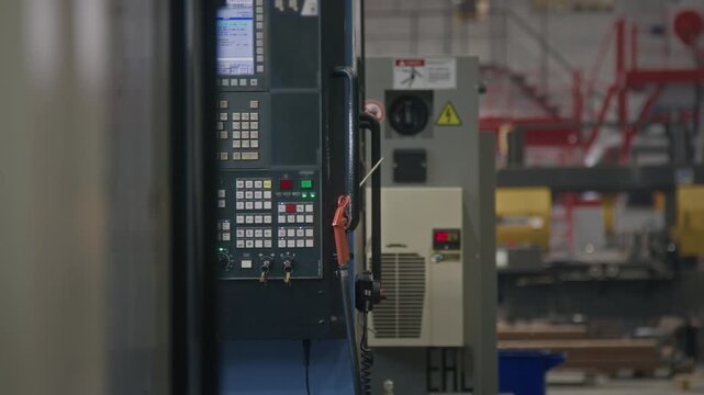 Interior of production plant with industrial control panel and factory workers walking in background