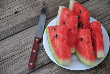 sliced watermelon on wooden table. plate with pieces of fresh ripe watermelon and knife on old wooden table.