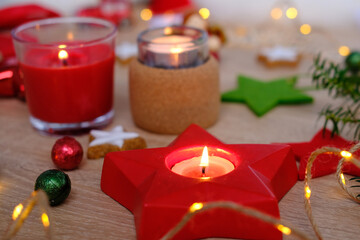 closeup decorated pre-Christmas table, candles are lit, garlands are lit, gift with red ribbon, concept of giving gifts to those close to holiday, festive mood, stars, sweets, cookies are scattered