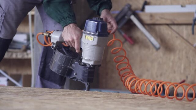 Woodworker uses pneumatic nail gun to hammer frame of wood hose building construction at workshop