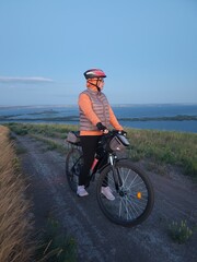 Naklejka premium A woman is cycling through nature against the background of a sunset.