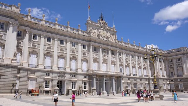 Royal Palace Madrid Spain Exterior. Crowds Walk In front Of White Spanish Building Summer Day Blue Sky and Clouds.