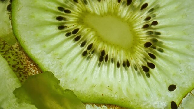 Macro shot of fresh juicy green kiwi slice moving against skylight, showing flesh and seeds with watery texture structure of fruit visible under light.