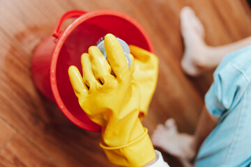 Person in yellow rubber gloves cleaning wooden floor with mop and bucket of water
