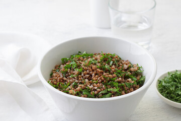 White bowl with boiled buckwheat and kale on a gray background, top view. Healthy homemade vegan food