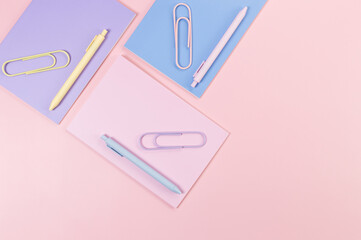 Top view of pink, purple and blue notebooks on pink background. Pink, yellow and blue pens, paperclips, school, office wallpaper. Flat lay, copy space.
