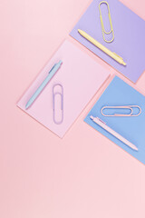 Top view of pink, purple and blue notebooks on pink background. Pink, yellow and blue pens, paperclips, school, office wallpaper. Flat lay, copy space.