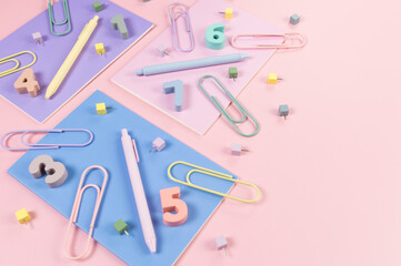 Top view of pink, purple and blue notebooks on pink background. Colorful pens, paperclips, numbers and pins. School, office wallpaper. Flat lay, copy space.