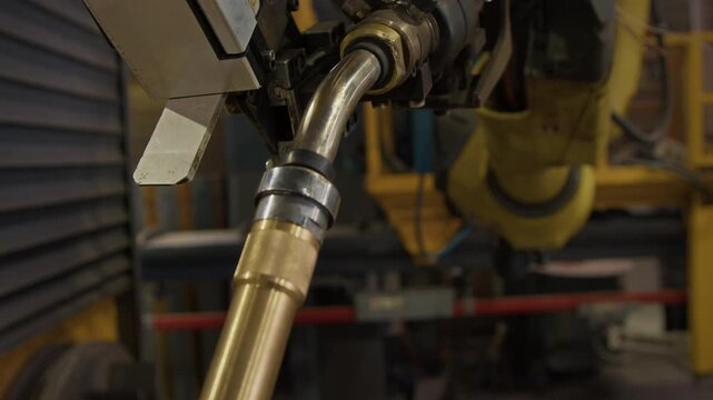 No people tilt closeup of stainless steel hand of yellow welding robot with build-in blowpipe in automated manufacturing plant, using computer-aided technologies