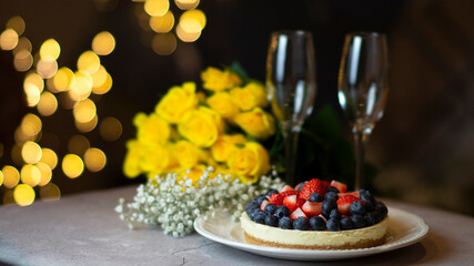 Cheesecake with berries close-up. Cake with strawberries and blueberries. Congratulations with flowers. Yellow roses and flutes on the table