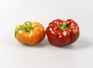 Close-up of two wet ugly fresh bell peppers with red and orange colors on white floor, South Korea
