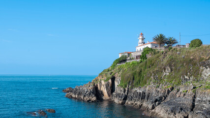 Hermoso faro marítimo sobre una punta de roca adentrándose en el mar Cantábrico en la villa de Cudillero, España © David Andres