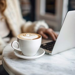 cup of coffee and laptop , cup of coffee with design of heart shape , white color , and laptop on the table.