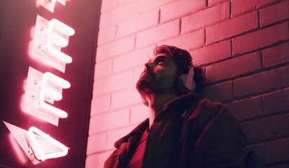 Man, relax and headphones at night outdoor for streaming music, inspiration podcast and listening to audio in city. Thinking, male person and ideas for playlist, entertainment and neon building © EmilLL/peopleimages.com