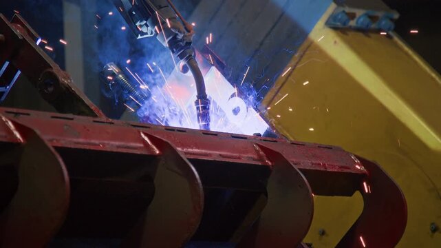 No people shot of computer-aided robotic welding arm welding metallic tractor parts in machinery production plant, using modern autonomous technologies